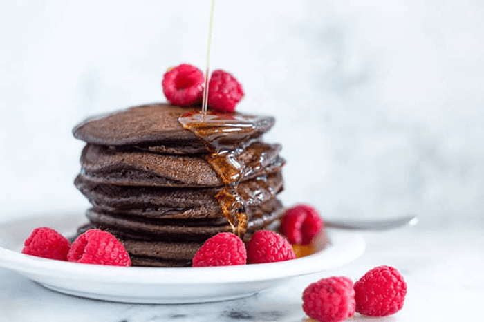 Finished plated Chocolate Protein Pancakes with raspberries and syrup.