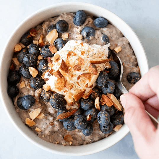 Finished bowl of blueberry crisp overnight oats with a hand scooping a spoonful of oats.