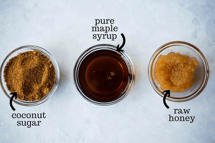 A photo of three bowls one has coconut sugar, one has maple syrup and another has raw honey.