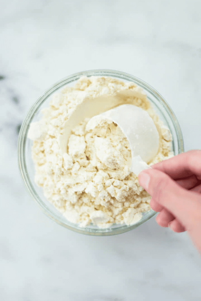 A picture of protein powder in a bowl, with a scoop of protein powder on top of it.