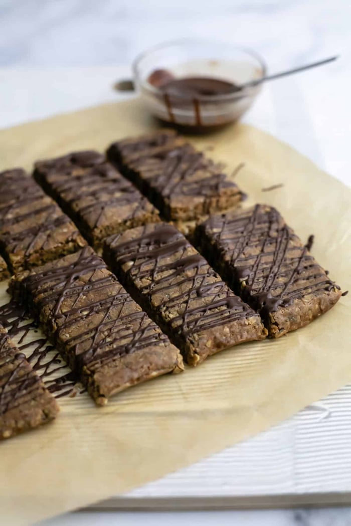 A photo of chocolate peanut butter protein bars on a piece of parchment paper with a chocolate drizzle.