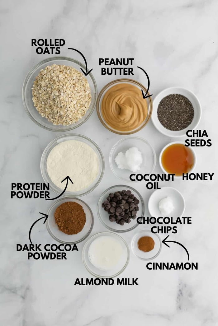 A photo of ingredients for chocolate peanut butter protein bars laying flat against a white marble surface.