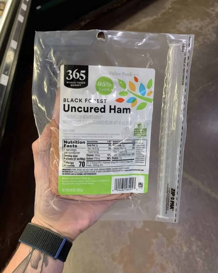A hand holding a package of deli meat branded 365 Whole Foods Market | Black Forest Uncured Ham.