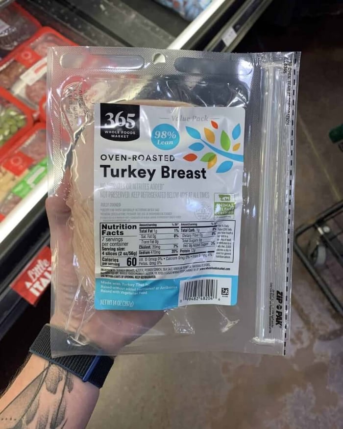 A hand holding a package of deli meat branded 365 Whole Foods Market | Oven-Roasted Turkey Breast..