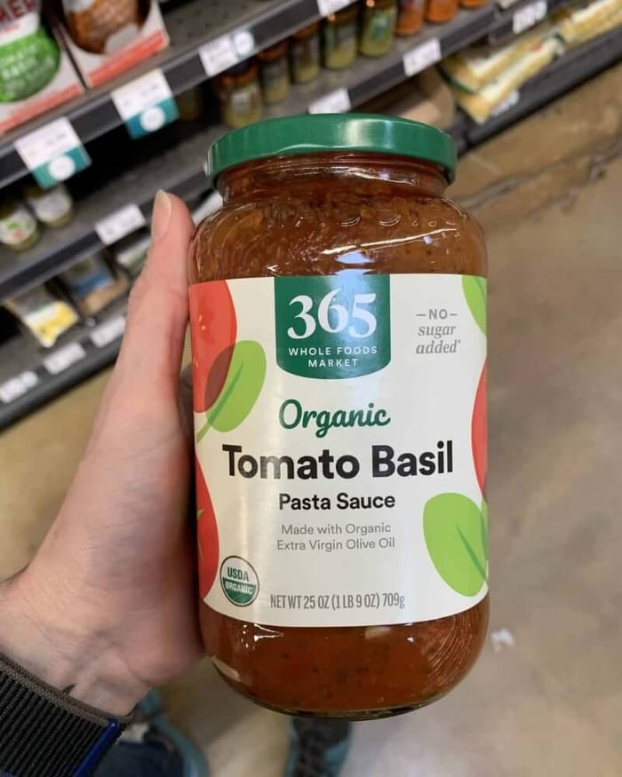 A hand holding a jar of pasta sauce branded by 365 Whole Foods.