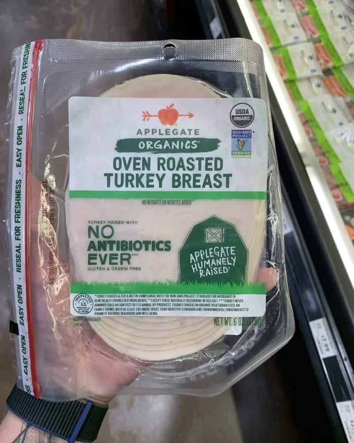 Hand holding a package of deli meat branded by Applegate Organic Turkey Breast.