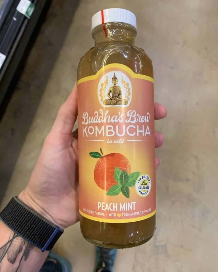 A photo of a hand holding a kombucha bottle labeled Buddha's Brew Kombucha.