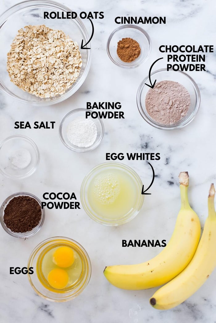A photo of ingredients for chocolate protein pancakes laying flat on a white marbled surface.