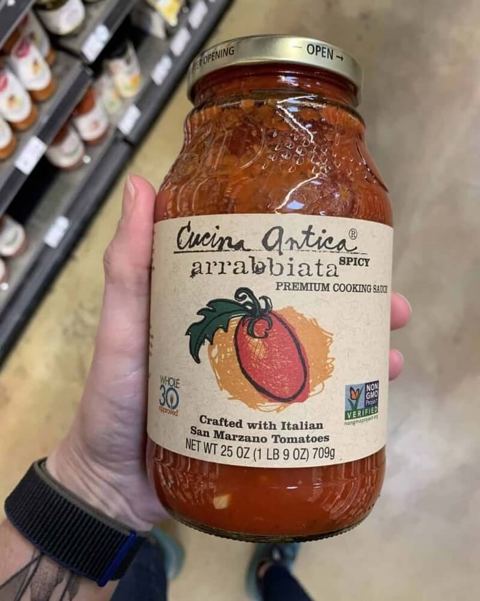 A hand holding a jar of pasta sauce branded by Cucina Antica.