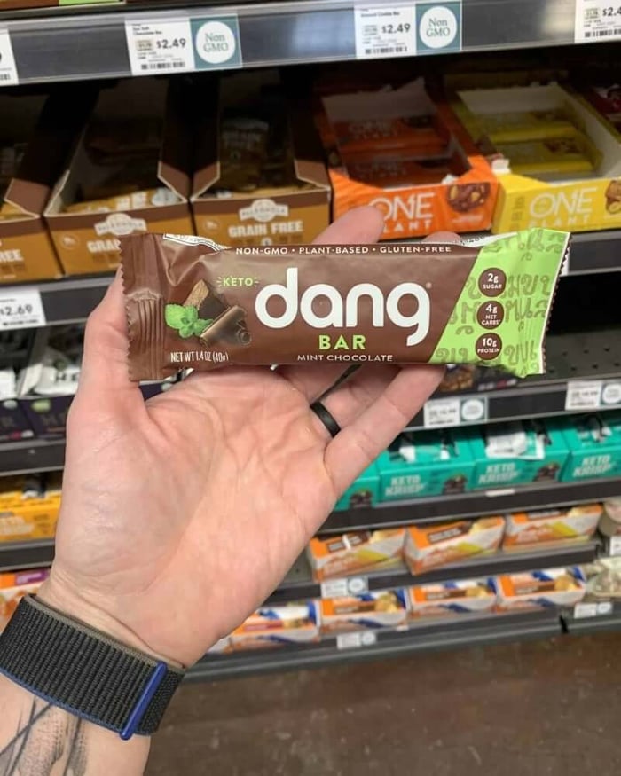 A hand holding a protein bar from the brand Dang.