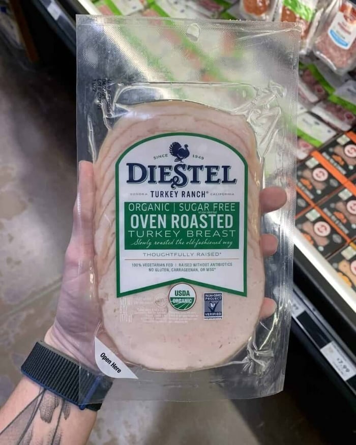 A hand holding a package of deli meat branded Diestel Oven Roasted Turkey Breast.