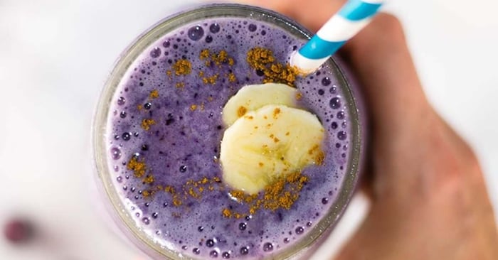 A cup full of blueberry protein smoothie with a blue and white straw.
