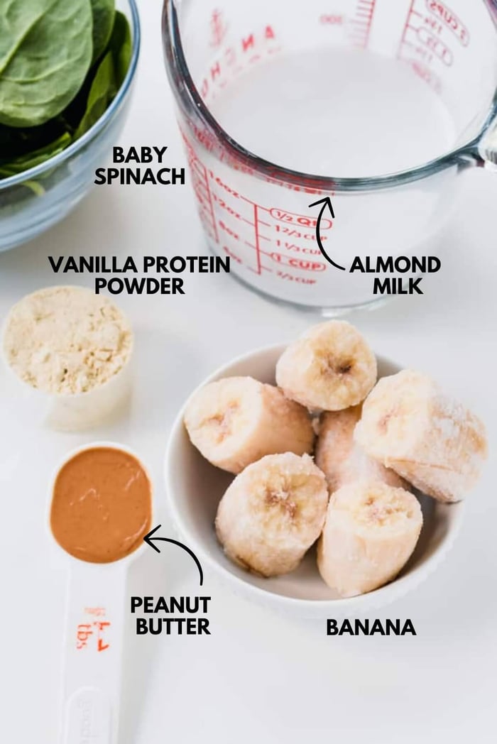 A photo of ingredients for green protein smoothie all laid out on a white marbled surface.