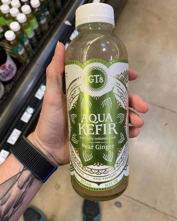 A photo of a hand holding a kombucha bottle labeled GT Aqua Kefir.