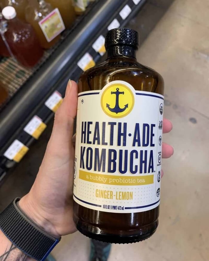 A photo of a hand holding a kombucha bottle labeled Health-Ade Kombucha.