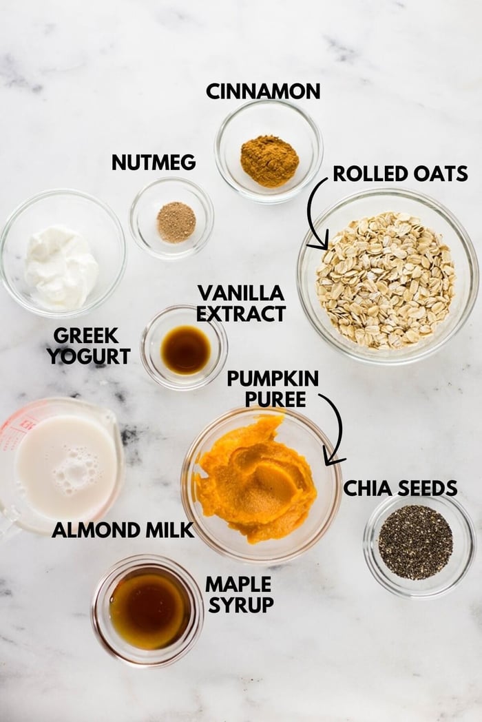 A photo of ingredients for pumpkin pie overnight oats laying flat against a white marbles surface.