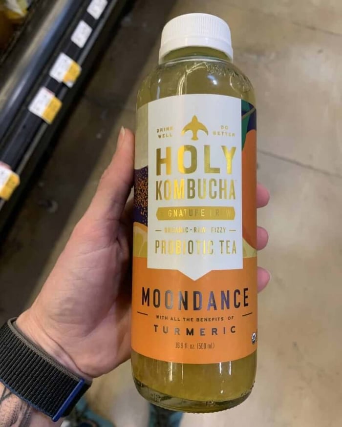 A photo of a hand holding a kombucha bottle labeled Holy Kombucha.