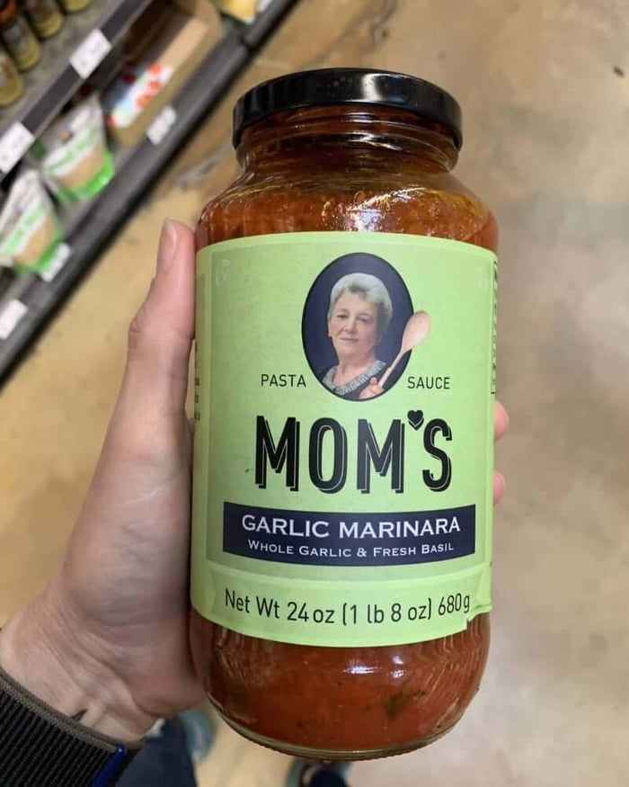 A hand holding a jar of pasta sauce branded by Mom's.