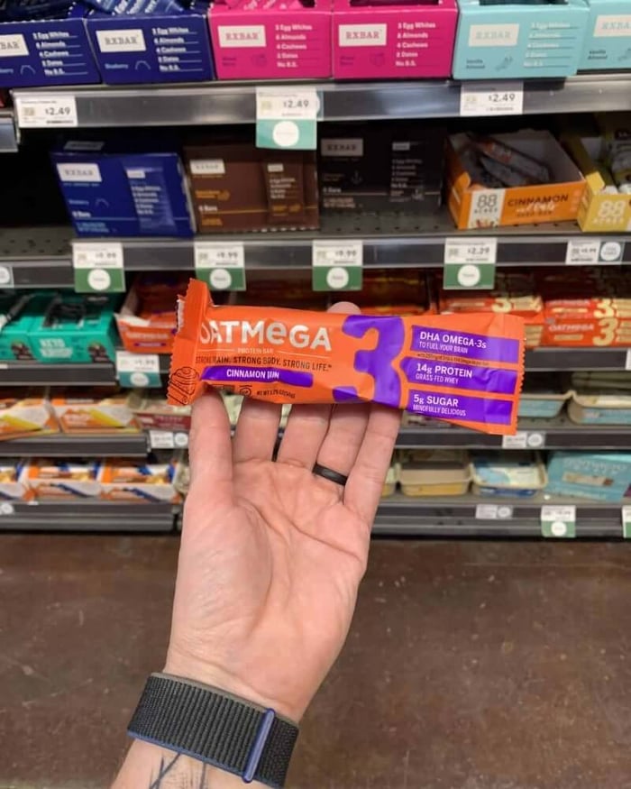 A hand holding a protein bar from the brand OatMega.