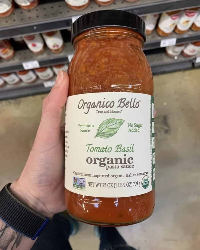 A hand holding a jar of pasta sauce branded by Organico Bello.