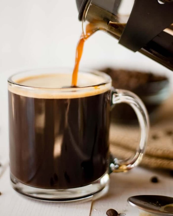 A photo of black coffee being poured into a clear glass mug.