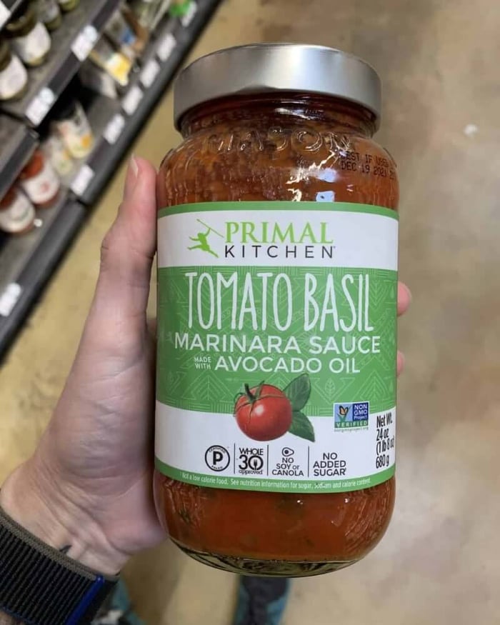 A hand holding a jar of pasta sauce branded by Primal Kitchen..
