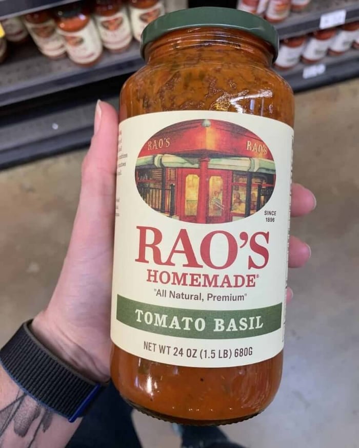 A hand holding a jar of pasta sauce branded by Rao's.