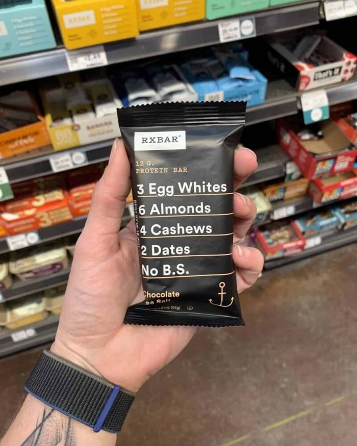 A hand holding a protein bar from the brand RXBar.