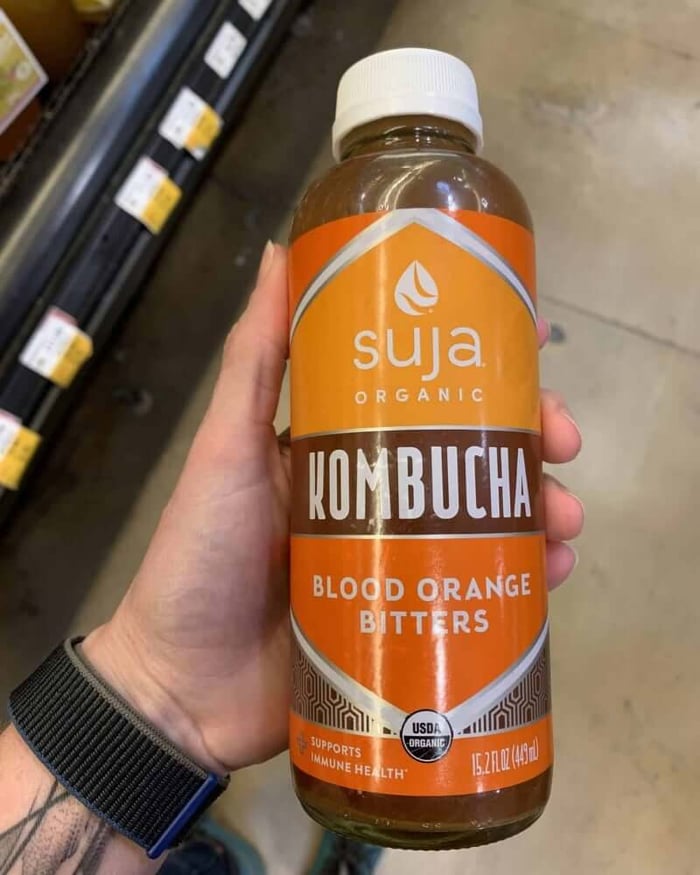 A photo of a hand holding a kombucha bottle labeled Suja Organic Kombucha.