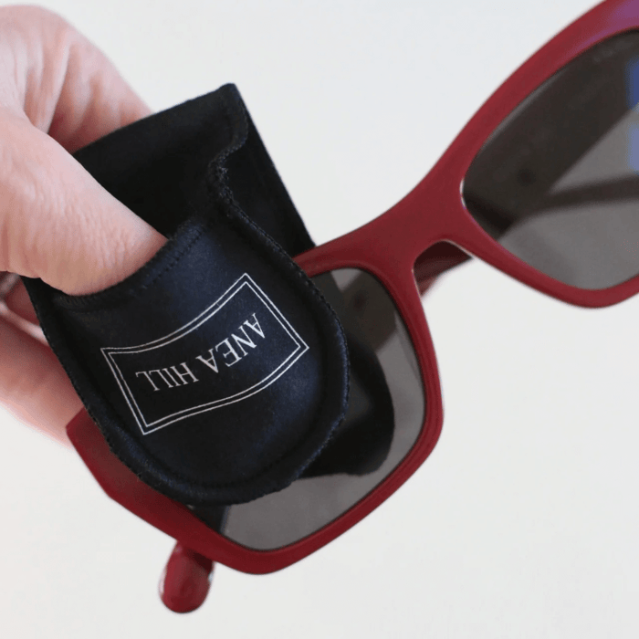 How to clean polarized sunglasses demonstration showing hand holding Anea Hill microfiber lens cleaning cloth with red polarized sunglasses