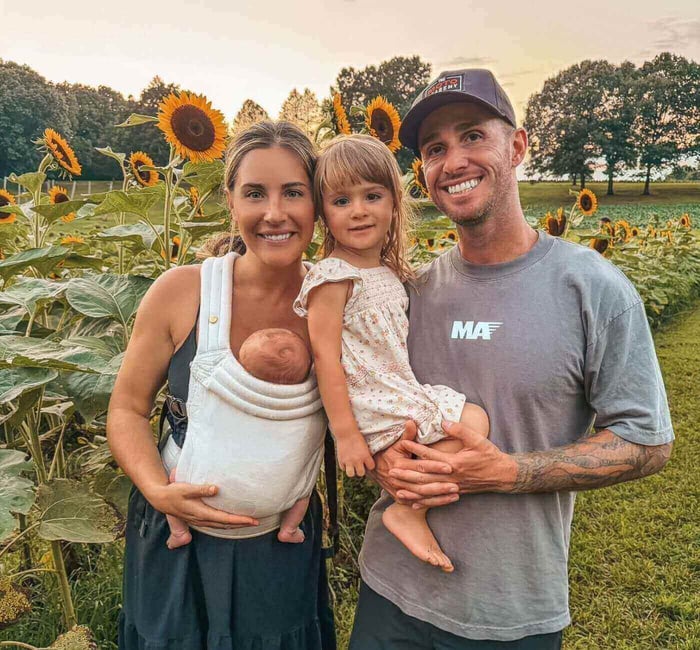 AJ and Ally Catanzaro with their two young children in a field of sunflowers.