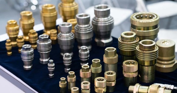 Assorted brass and steel pneumatic couplers and fittings in various sizes arranged upright on a dark display surface.