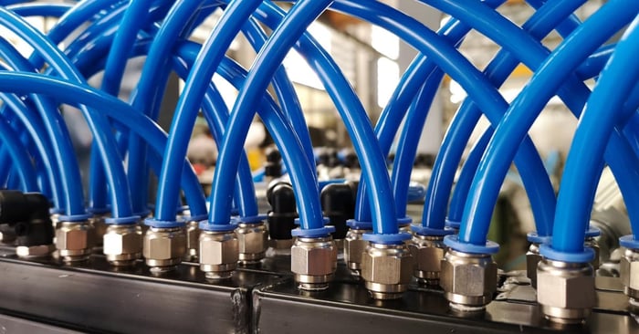 Blue pneumatic tubes curve into metal push-to-connect fittings mounted along a black industrial air manifold.