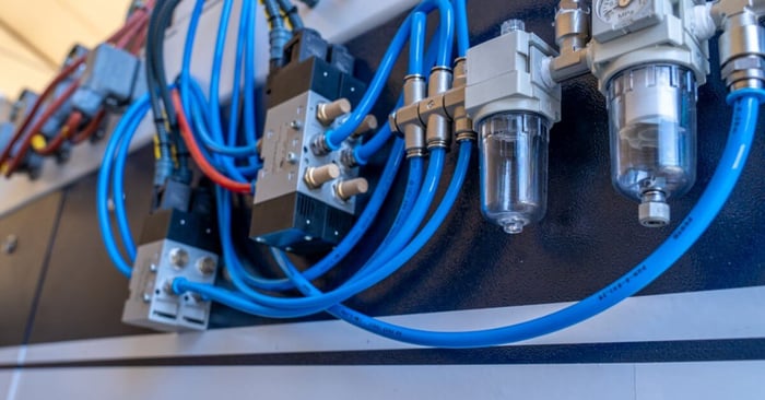 Compressed air filter regulator and blue pneumatic hoses connected to industrial control valves on automated machinery panel.