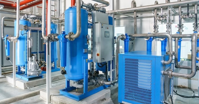 A blue refrigerated air dryer for compressed air connected to multiple steel pipes in an industrial setting.