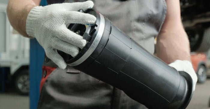 An individual in a gray and red uniform and white gloves holding a black and silver pneumatic air cylinder.