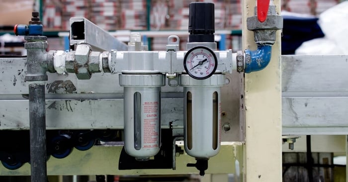 A silver and black pneumatic air filter with a numbered gauge attached to a piece of industrial equipment.
