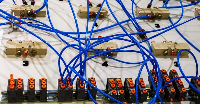 A complex pneumatic system with blue tubes connecting beige solenoid valves and black manifold blocks on a labeled panel.