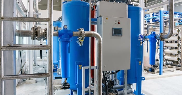 Two large blue tanks, silver pipes, and control panels dominate an industrial water treatment system in a clean facility.