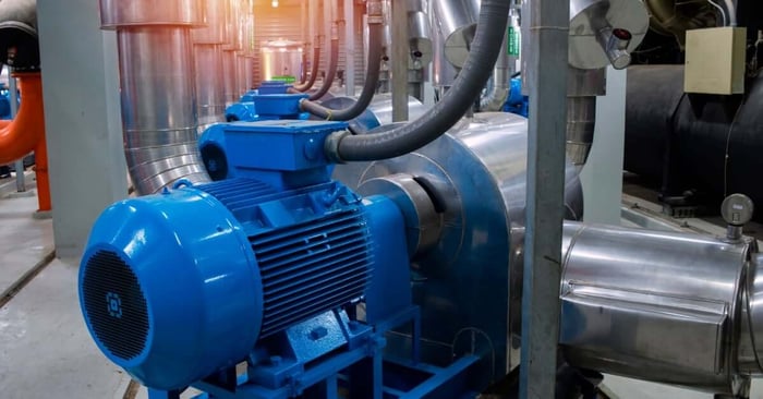 A blue industrial air compressor connected to stainless steel piping inside a large mechanical plant room.