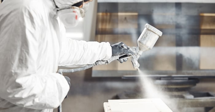 A worker standing beside a yellow portable air compressor in a renovation space, holding a hard hat and ear protection.