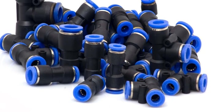 A pile of black push-to-connect pneumatic fittings with blue release rings, stacked together on a white background.