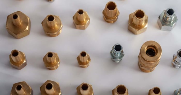 Various brass and steel pneumatic hose fittings and connectors arranged in rows on a white background.