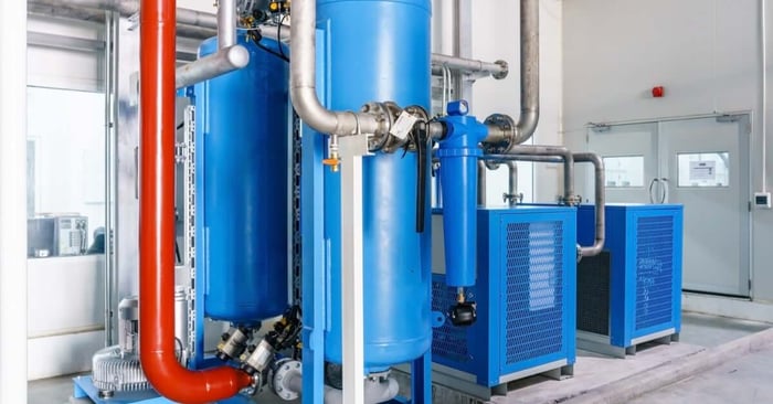 Large blue vertical air tanks and dryers connected by silver and red piping in a clean industrial mechanical room.
