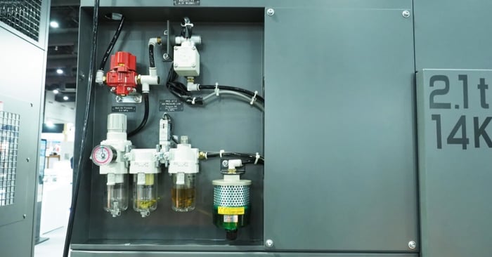 An industrial air filtration and regulator assembly with a pressure gauge, multiple filter bowls, and tubing.