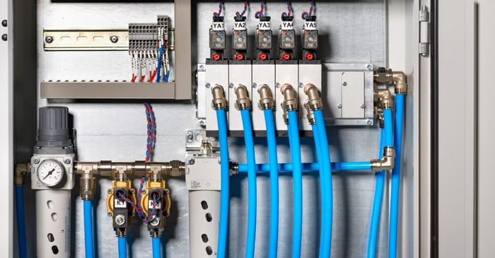 A pneumatic control panel with blue air hoses, solenoid valves, wiring terminals, and filtration components.