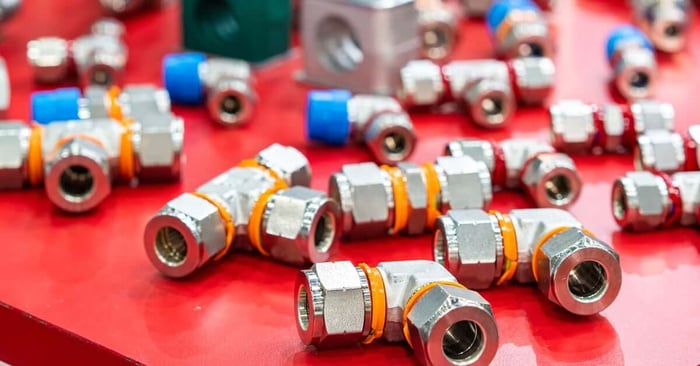 Metal pneumatic air fittings with orange and blue seals arranged on a red display surface in an industrial setting.