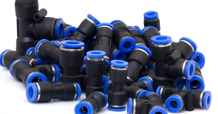 A pile of black and blue push-to-connect pneumatic air fittings displayed on a white background for air systems.