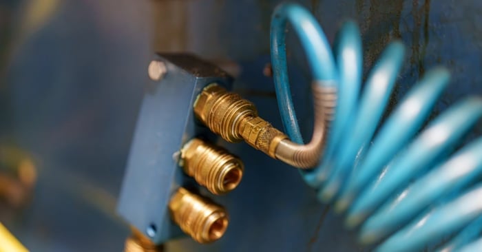 A blue coiled air hose connected to brass quick-connect pneumatic fittings mounted on an industrial equipment panel.