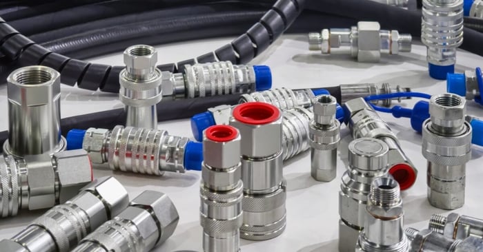 Assorted silver pneumatic quick-connect couplings and hose fittings arranged beside coiled industrial hydraulic hoses.